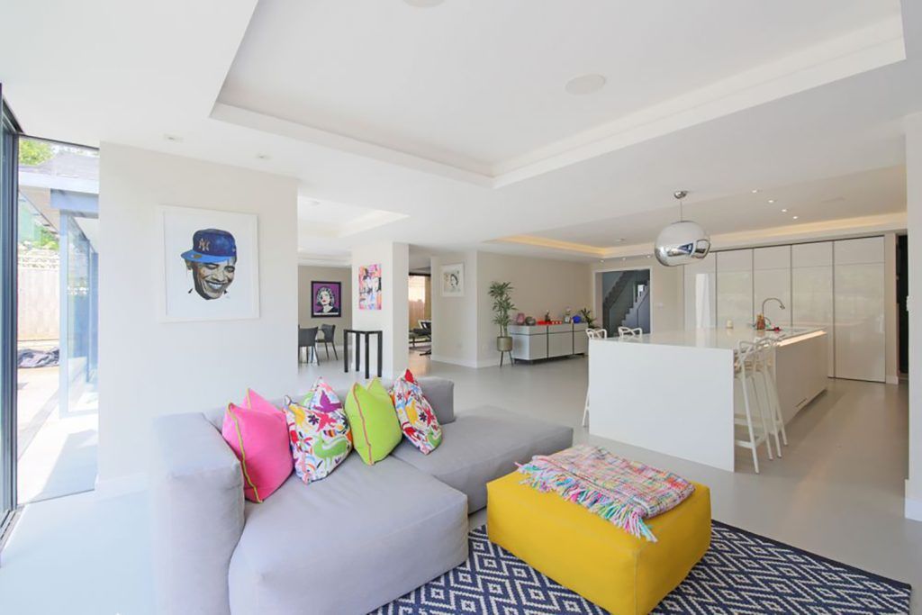 Modern white extension with concrete flooring, white kitchen island, grey sofa and yellow footstool. 