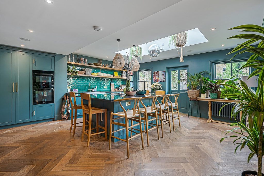 A deep blue modern kitchen with parquet flooring, a kitchen island with six wooden bar stools.