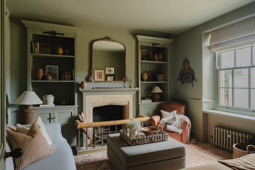 a cosy living room with light green walls, built-in bookshelves and a fireplace.